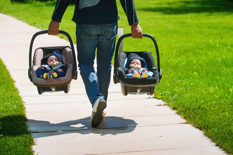 Father carrying twin babies in car seats family time together