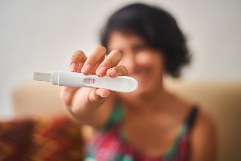 Happy young latina woman shows positive pregnancy test. Concept, conscious motherhood, family planning.